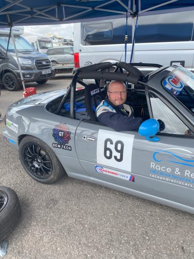 A driver seated in a grey racing car with the number 69, prepared for a race.