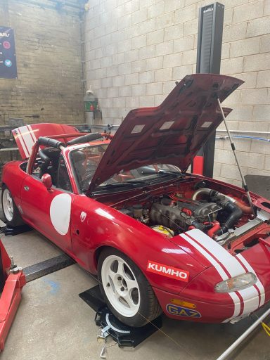 Red sports car with an open hood, lifted for inspection in a workshop setting.